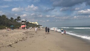 A beach with people walking and relaxing. There are umbrellas and beach chairs.