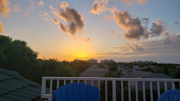 A balcony with a view of a sunset over a residential area, featuring houses and greenery.