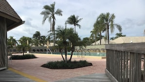 A wooden deck leading to a pool area with palm trees and lounge chairs.