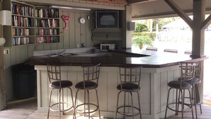 A kitchen with a bar area, bookshelves, a clock, and a television.