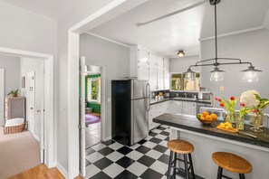 Une cuisine avec un sol à carreaux noirs et blancs, un réfrigérateur en acier inoxydable et un coin bar avec des tabourets.