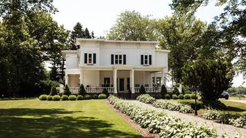 Stately two-story building with a central entrance and covered porch, set amidst a beautifully manicured lawn and lush greenery.