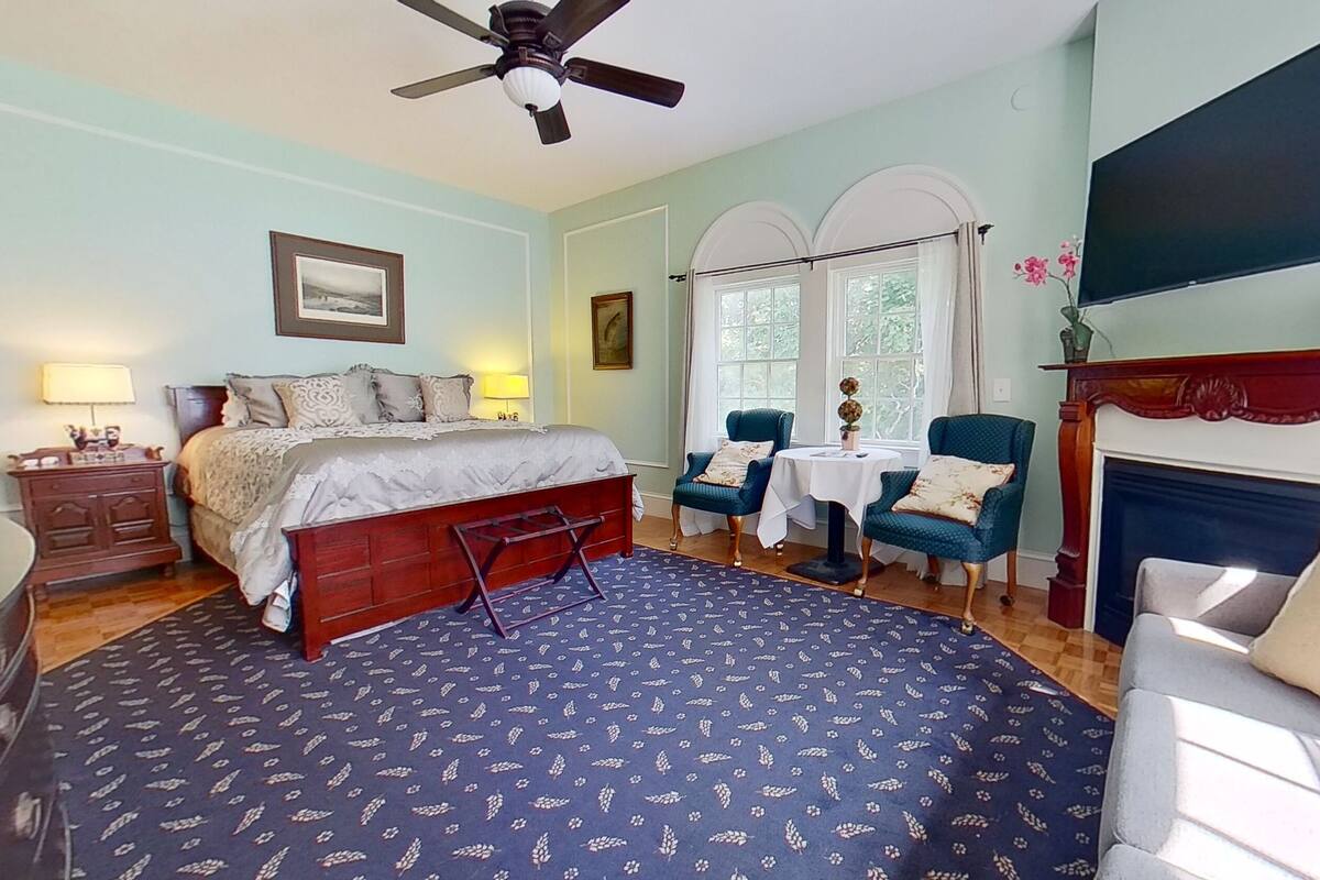 Une chambre à coucher comprenant un lit, un bureau, une chaise, une cheminée et une fenêtre.