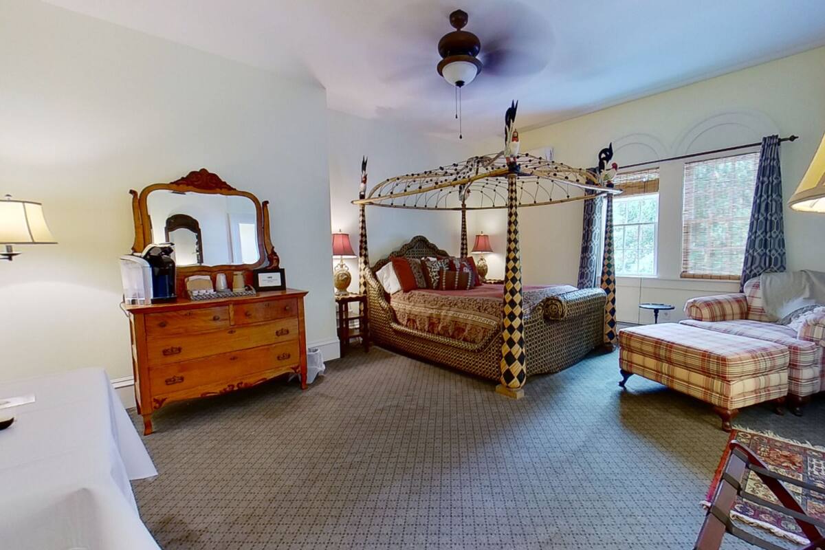 Une chambre à coucher avec un lit à baldaquin, une commode, une chaise et une fenêtre avec des rideaux.