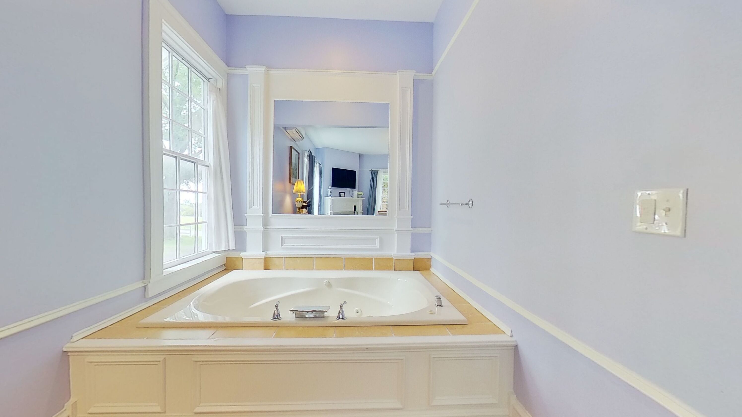 A bathroom with a large bathtub, a window, and a mirror.