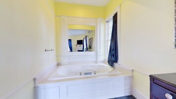 Un baño con una bañera blanca, un espejo encima y una ventana con cortinas.