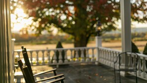 A porch with a railing, a bench, and a chair. - John Joseph Inn (Groton)