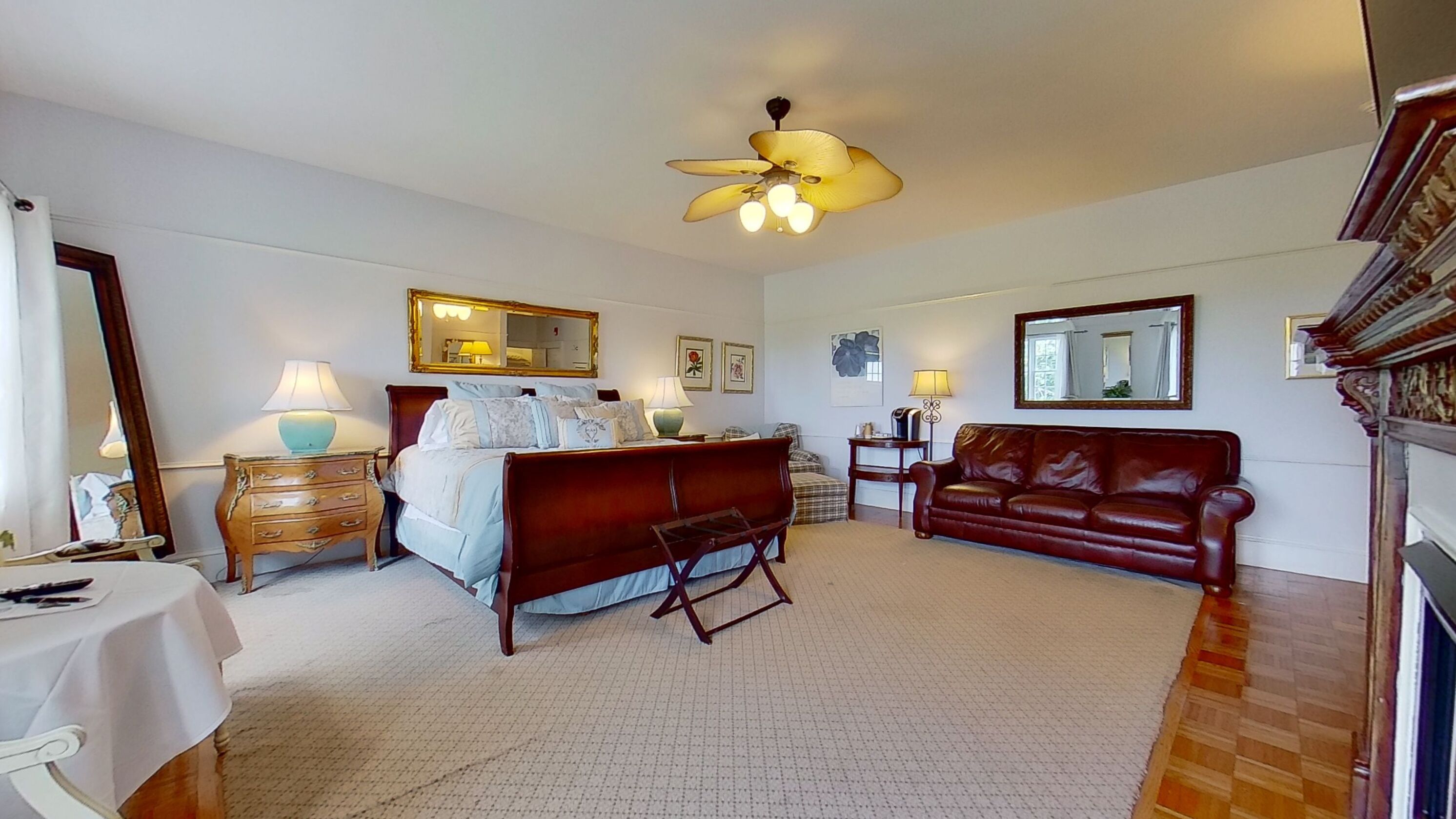 A bedroom with a bed, a wooden bench, a leather sofa, a ceiling fan, and two bedside tables with lamps.