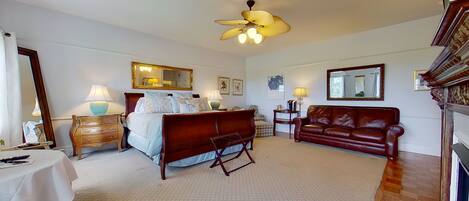 A bedroom with a bed, a wooden bench, a leather sofa, a ceiling fan, and two bedside tables with lamps.