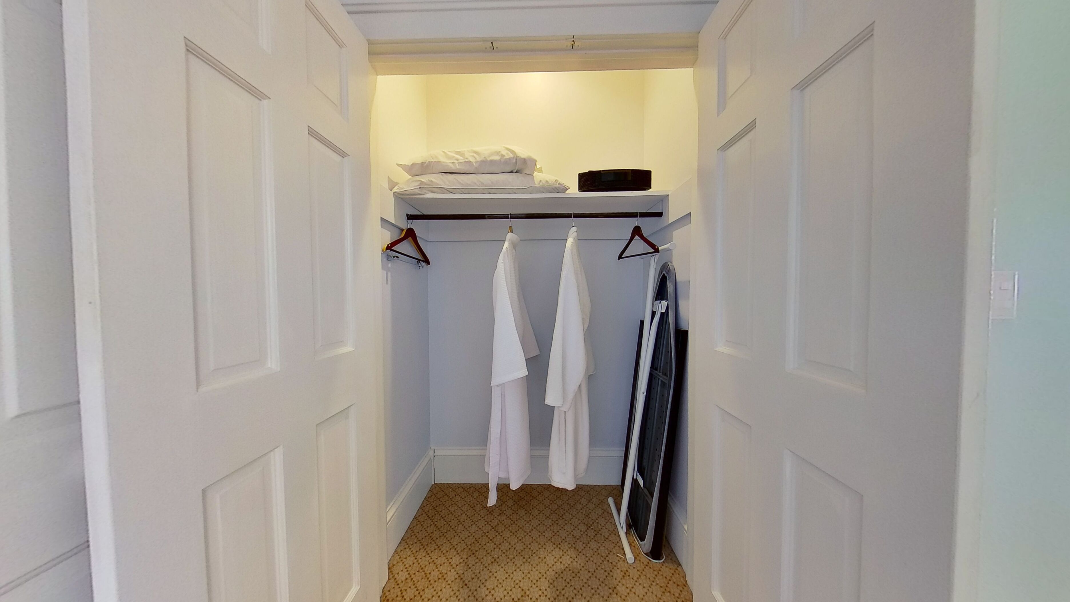 A narrow hallway with a closet containing a bed, a shelf with items, and a drying rack with clothes.