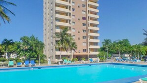 A swimming pool with lounge chairs and palm trees, surrounded by a tall building. - Coconut Suite at Turtle Towers (Ocho Rios)