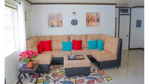 A living room with a beige sectional sofa, colorful cushions, a small side table with a potted plant, and a patterned rug. - Coconut Suite at Turtle Towers (Ocho Rios)