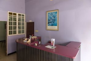 Un comptoir d’accueil avec un plan de travail violet, une citation encadrée accrochée au mur et une fenêtre avec des stores.