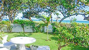 A white outdoor seating area with a table and chairs, surrounded by greenery and a view of the ocean. - Villa Island Breeze (Duncans)