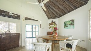 A dining area with a round wooden table, white wicker chairs, and a ceiling fan. - Villa Island Breeze (Duncans)
