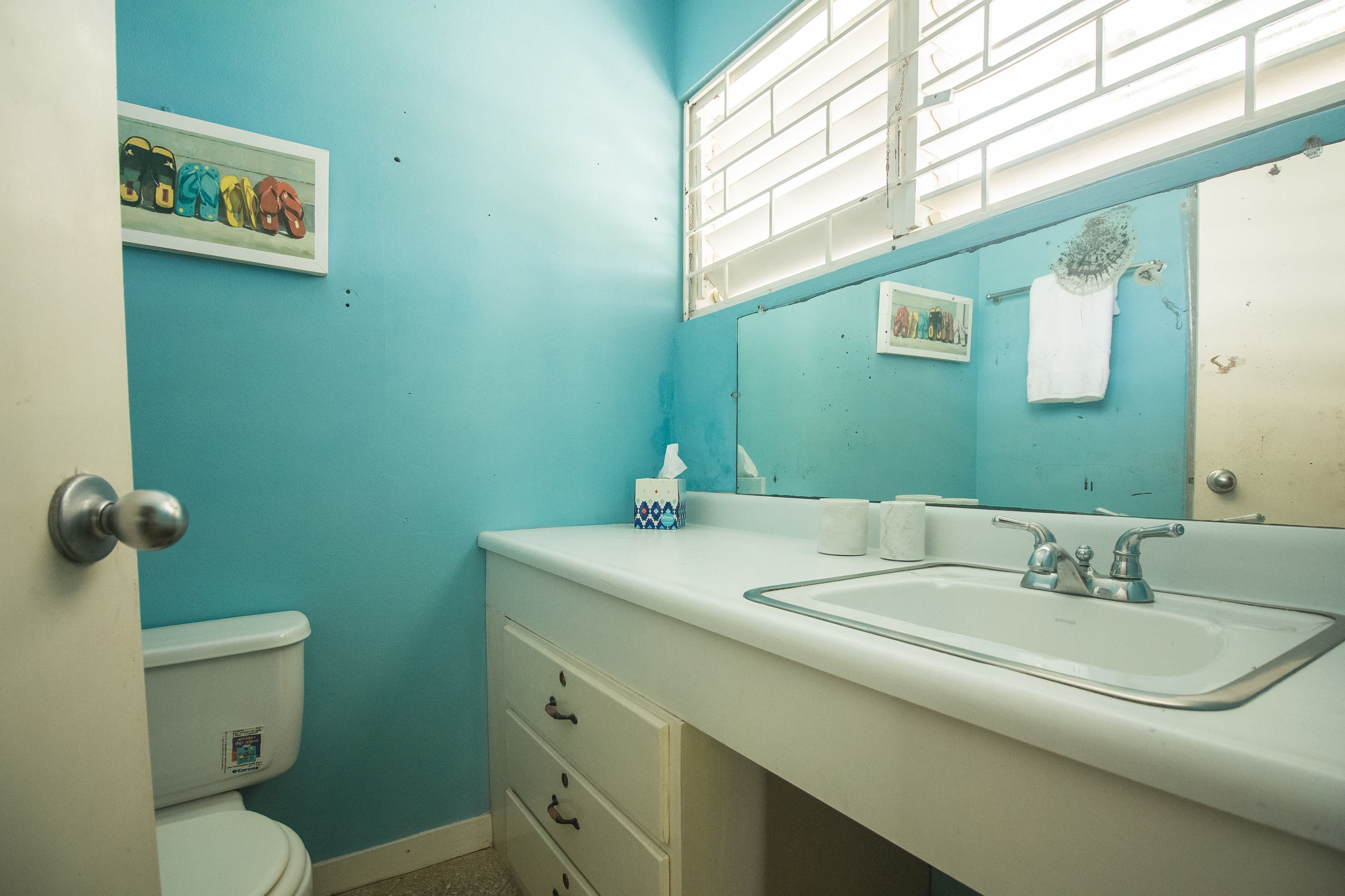 Um banheiro com parede azul, pia branca e vaso sanitário.