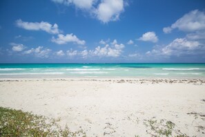 A beach with clear turquoise water and a sandy shore under a blue sky with scattered clouds. - Villa Island Breeze (Duncans)