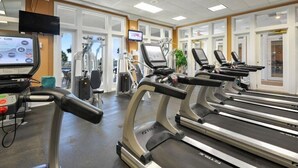 Ein Fitnessstudio mit Laufbändern, Trainingsgeräten und einem Fernsehbildschirm, der Trainingsmöglichkeiten zeigt.