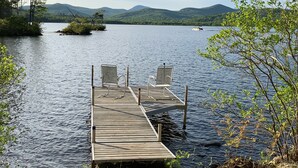 Une jetée en bois s’avance sur un lac paisible, avec deux chaises vides qui donnent sur l’eau.