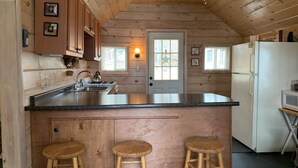 A kitchen with wooden walls, a large island with stools, a refrigerator, and a window with a view.