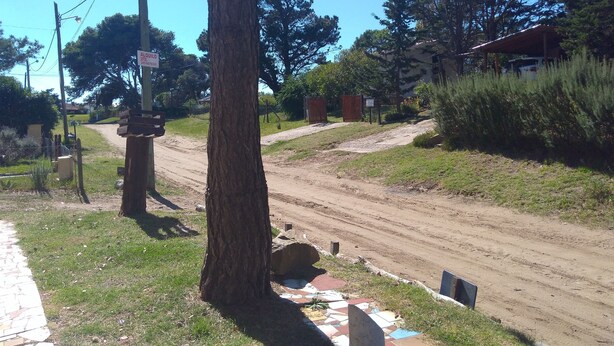 Un camino de tierra con una cerca de madera y un árbol a la izquierda. Hay un cartel con un número de teléfono en un poste.
