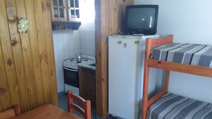 Una cocina pequeña con estufa, lavaplatos y refrigerador, una mesa de madera y una cama litera con ropa de cama a rayas.