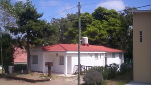Una pequeña casa de un solo piso con techo rojo, rodeada de follaje y árboles.