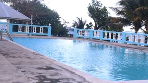 Una piscina con ringhiera blu, circondata da alberi e un edificio con tetto blu.