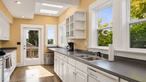 A modern kitchen with white cabinets, a dishwasher, a coffee maker, and a window with a view of greenery. - Seattle Vacation Home: The Campus (Seattle)