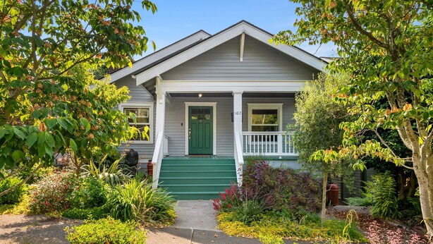 A two-story house with a green front door, white porch railing, and a small front yard with various plants and a pathway leading to the door. - Seattle Vacation Home: The Campus (Seattle)