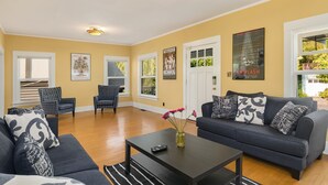 A living room with a dark blue sofa, a coffee table, and a vase with flowers. There are two armchairs and a rug on the floor. - Seattle Vacation Home: The Campus (Seattle)