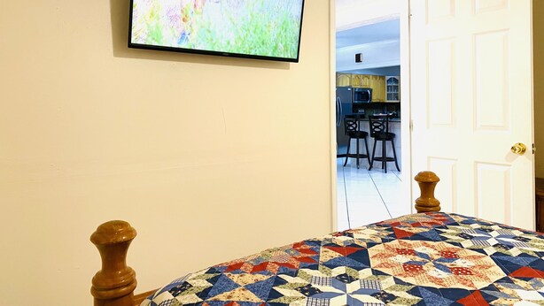 Un dormitorio con una cama, un televisor montado en la pared y una puerta que da a una zona de cocina.