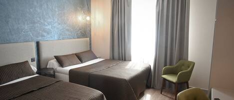 Una habitación de hotel con dos camas, un sillón verde, un control remoto y un ventanal con cortinas.