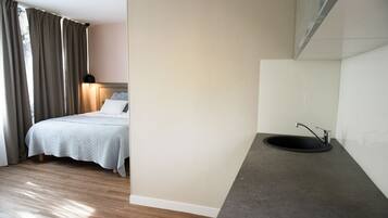 A bedroom with a bed, bedside lamp, and a bathroom with a sink and mirror.