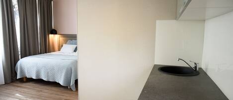A bedroom with a bed, bedside lamp, and a bathroom with a sink and mirror.
