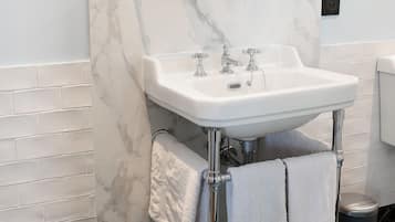 Un baño con un lavamanos blanco, un espejo redondo y dos toallas colgadas en la pared.