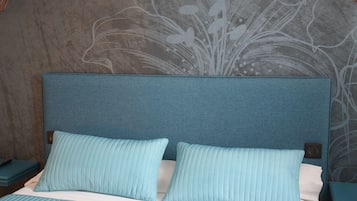 Una cama con cabecera azul y almohadas a juego, una colcha blanca y una pared con estampado floral.