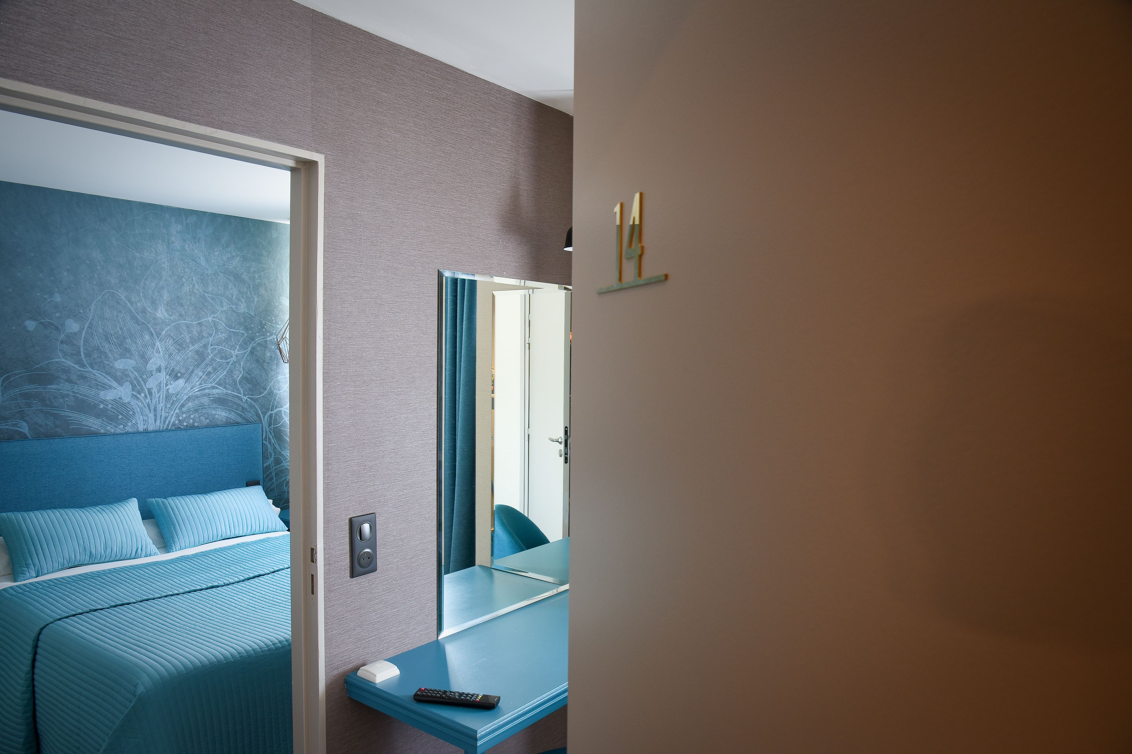 A modern hotel room with a bed, a bedside table, a mirror, and a wall-mounted shelf.