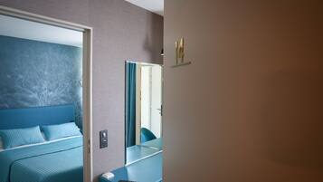 A modern hotel room with a bed, a bedside table, a mirror, and a wall-mounted shelf.