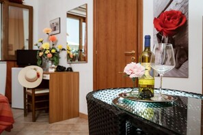 A room with a dining table set with a bottle of wine and a glass, a vase with flowers, a hat on a chair, and a wooden cabinet. - B&B Panorama (Castelbuono)