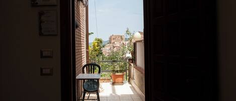 A porta aberta dá para uma varanda com uma cadeira e plantas em vasos.