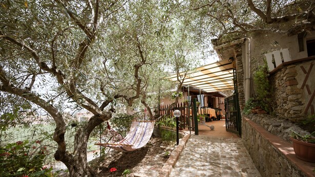 A stone pathway leading to a covered outdoor seating area with a hammock and a view of a garden with red flowers. - B&B Panorama (Castelbuono)