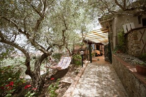 A stone pathway leading to a covered outdoor seating area with a hammock and a view of a garden with red flowers. - B&B Panorama (Castelbuono)