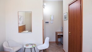 A small, clean room with a wooden desk, a chair, a small table, a mirror, and a door. - B&B Panorama (Castelbuono)