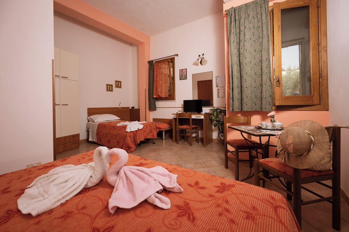 Habitación de hotel con cama, escritorio, silla, ventana con cortinas, armario y espejo.