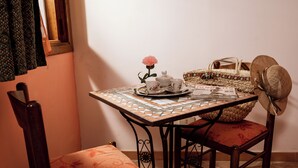 A small dining table with a patterned tablecloth, a floral vase, and a magazine. There is a wicker basket and a straw hat on the table. - B&B Panorama (Castelbuono)