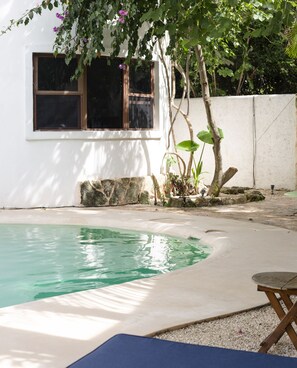 A swimming pool with a stone edge, a wooden deck, and a window with a view of the surrounding greenery. - Sonido Del Mar Hotel and Yoga Loft (Tulum)