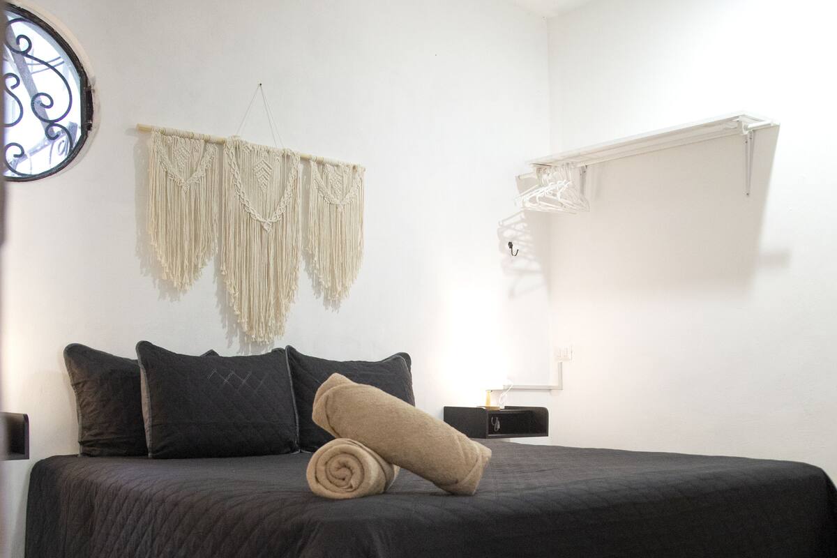 Un lit avec une couverture sombre, deux oreillers et une serviette enroulée.