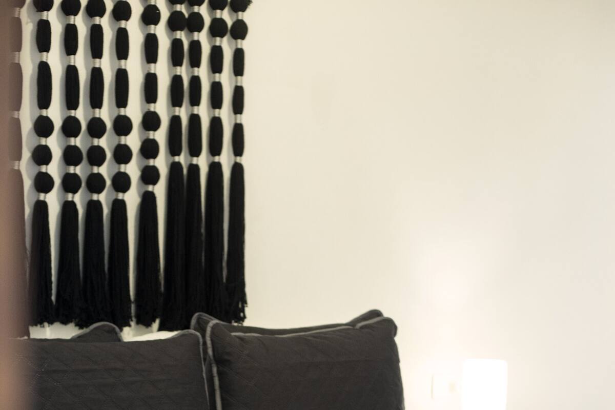 Un lit recouvert d’une couvre-lit noire et blanche, deux oreillers noirs, une tête de lit en bois et une table de chevet avec une lampe.
