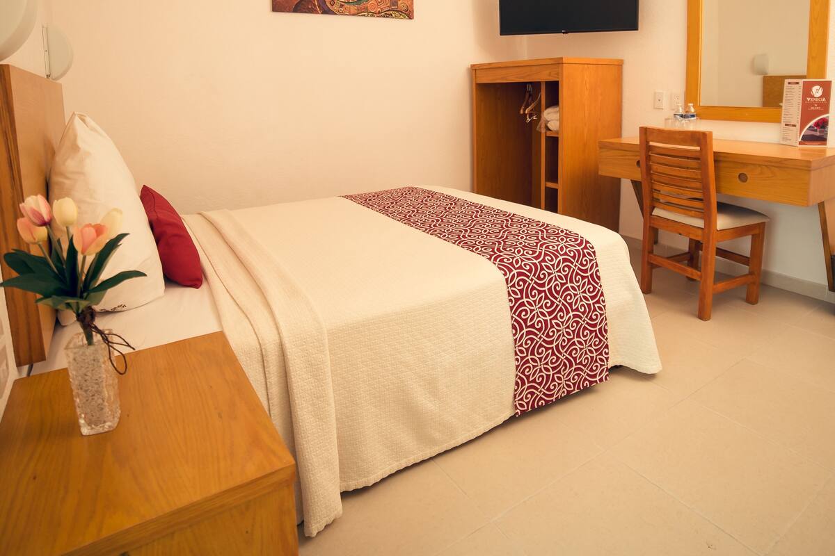 Ein Hotelzimmer mit einem Bett, einem Schreibtisch mit Stuhl, einem Fernseher und einem Spiegel.